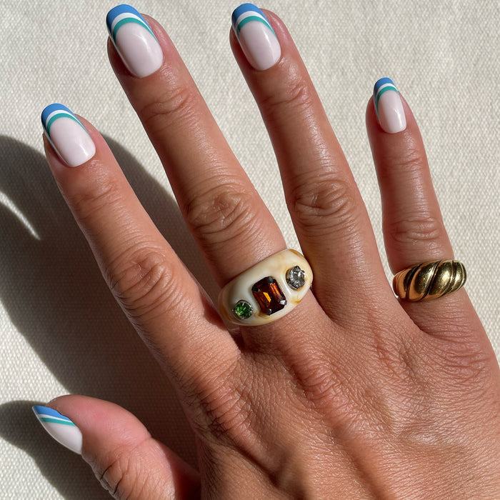 Hand with Triple French | Round | Short press-on manicure featuring blue and green triple stripes on pale base in sunlight