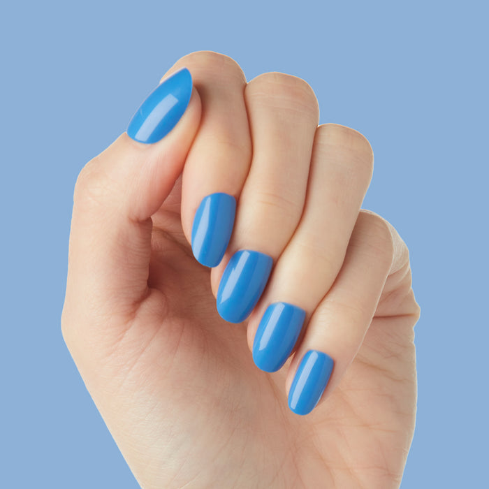 Hand displaying Blue Canoe | Round | Short press-on nails in medium denim blue with glossy finish on blue background