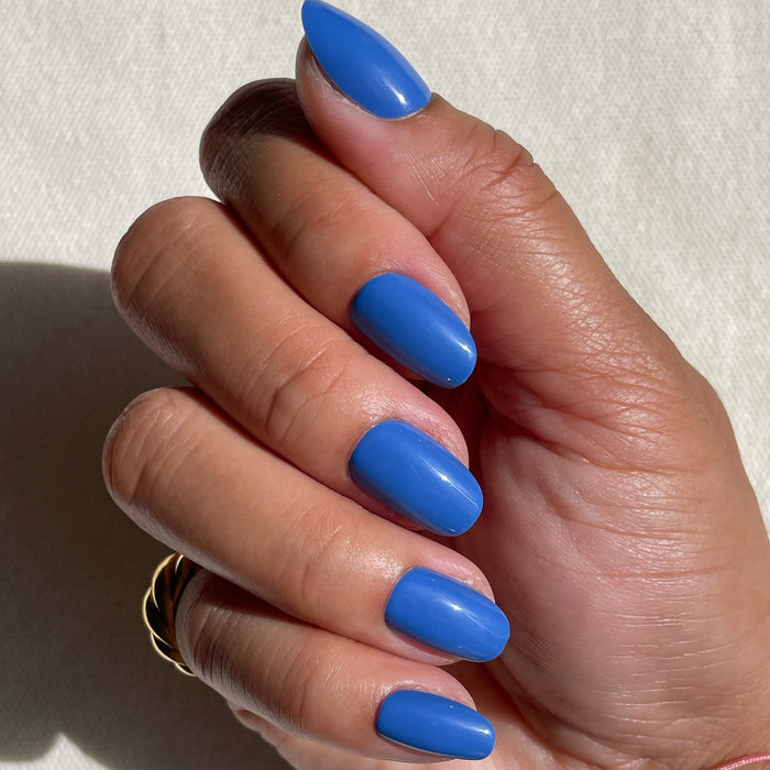 Hand with Blue Canoe | Round | Short press-on nails in rich medium denim blue glossy finish on natural skin tone against light background