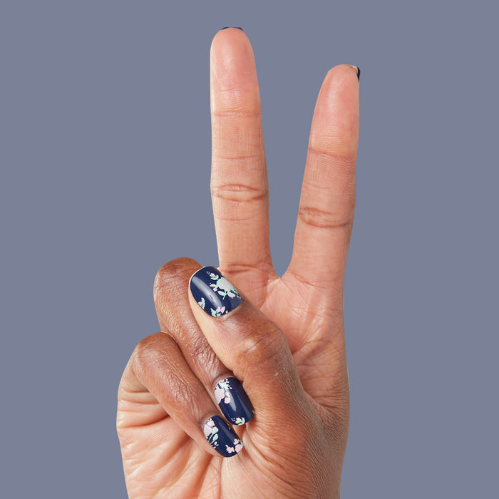 Hand showing two fingers with Micro Floral - Press-Ons | Extra Short | Squoval featuring white flowers on dark navy nails