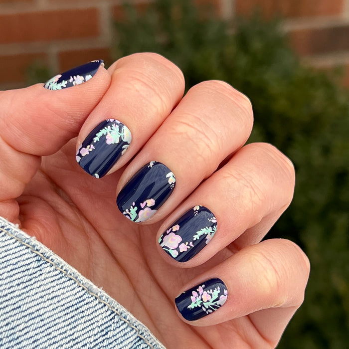 Hand displaying Micro Floral - Press-Ons | Extra Short | Squoval with pastel floral design on dark navy base for spring mani