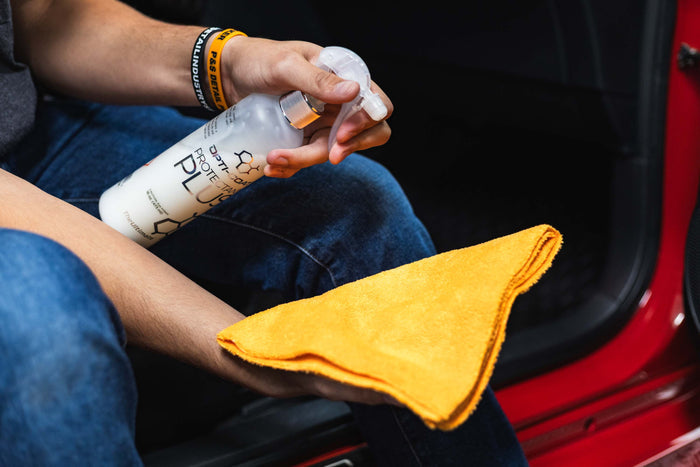 Person cleaning a car with Opti-Coat Protectant Plus and a orange microfiber.
