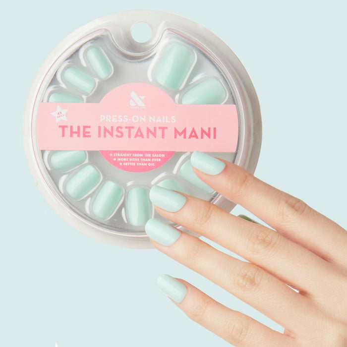 Hand wearing Sleeping Bag | Squoval | Short pastel mint green press-on nails with packaging on light blue background
