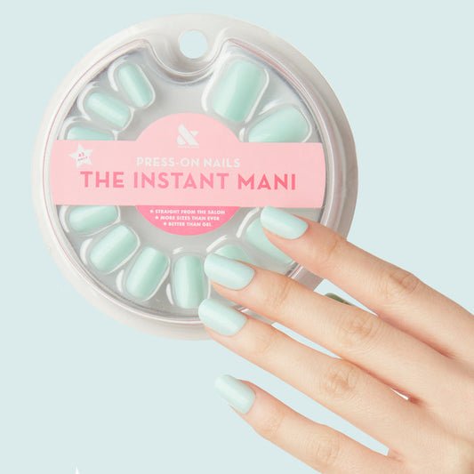 Hand wearing Sleeping Bag | Squoval | Short pastel mint green press-on nails with packaging on light blue background