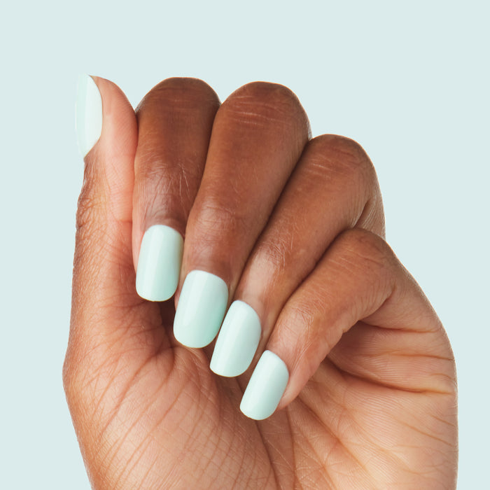Hand with Sleeping Bag | Squoval | Short mint pastel green press-on nails on medium skin tone against pale blue background