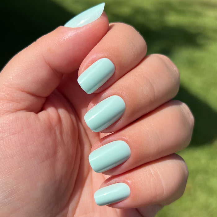 Hand displaying Sleeping Bag | Squoval | Short mint pastel green press-on nails in natural sunlight outdoors