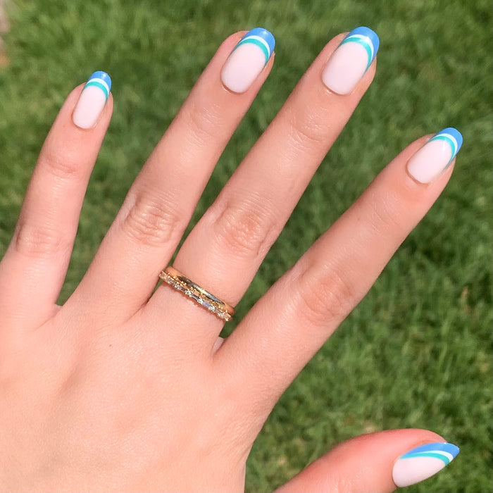 Hand with Triple French | Round | Short press-on mani showing blue and green triple stripe tips on pale base outdoors