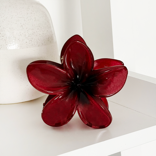 Burgundy Tropical Flower Claw Clip next to a red glass flower ornament and speckled vase on a white shelf.