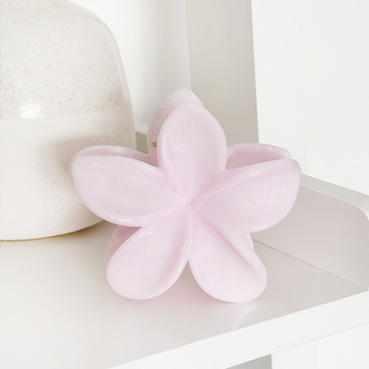 Powder pink tropical flower claw clip from Coconut Lane on a white shelf next to a speckled ceramic vase.