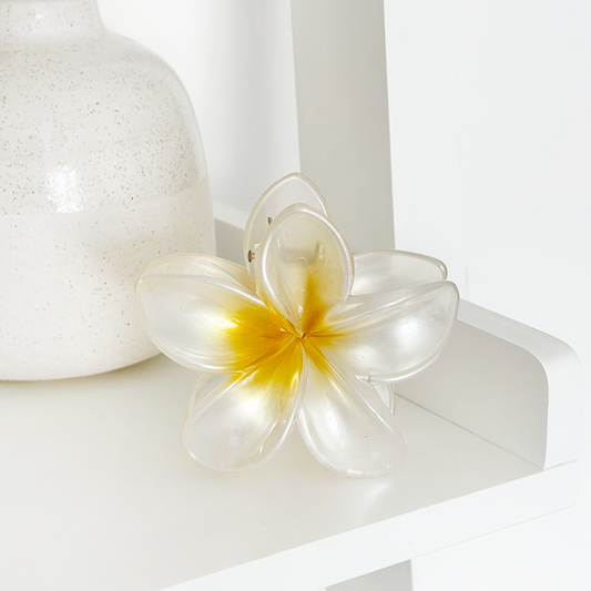 White and yellow tropical flower claw clip by Coconut Lane on a white shelf beside a speckled vase.