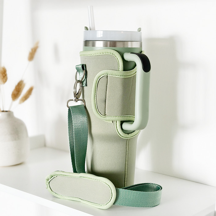 Soft sage Coconut Lane tumbler carry case on a white shelf beside a vase of dried grasses.